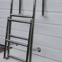 Polerowana, metalowa drabinka basenowa, przymocowana do białej ściany z panelami, leżąca na białej płycie.