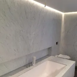 Wykończona łazienka w Biłgoraju z wanną obudowaną białym marmurem, oświetleniem LED w suficie i ścianach wyłożonych marmurowymi płytami z widocznym wzorem żyłkowania.