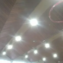 Wnętrze hali sportowej z drewnianym sufitem i rzędem jasnych lamp, w tle widoczny fragment kosza do gry.