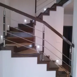 Nowoczesne schody z ciemnego drewna i metalowymi balustradami, oświetlone punktowymi lampkami w ścianie.