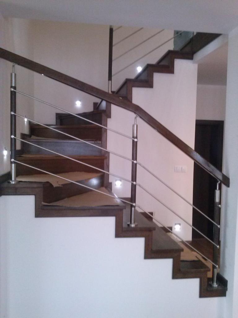 Nowoczesne schody z ciemnego drewna i metalowymi balustradami, oświetlone punktowymi lampkami w ścianie.