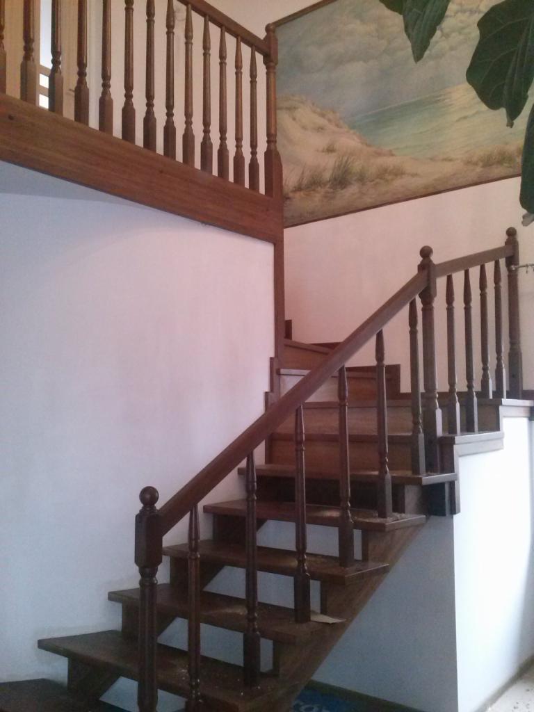 Drewniane schody z balustradą w tradycyjnym stylu, z dekoracyjnym malowidłem na ścianie przedstawiającym pejzaż morski.