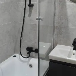 Nowoczesna łazienka: biała wanna z czarną armaturą, szklany parawan, umywalka z szafką w odcieniach szarości i okrągłe lustro. Minimalistyczny design i stonowana kolorystyka.