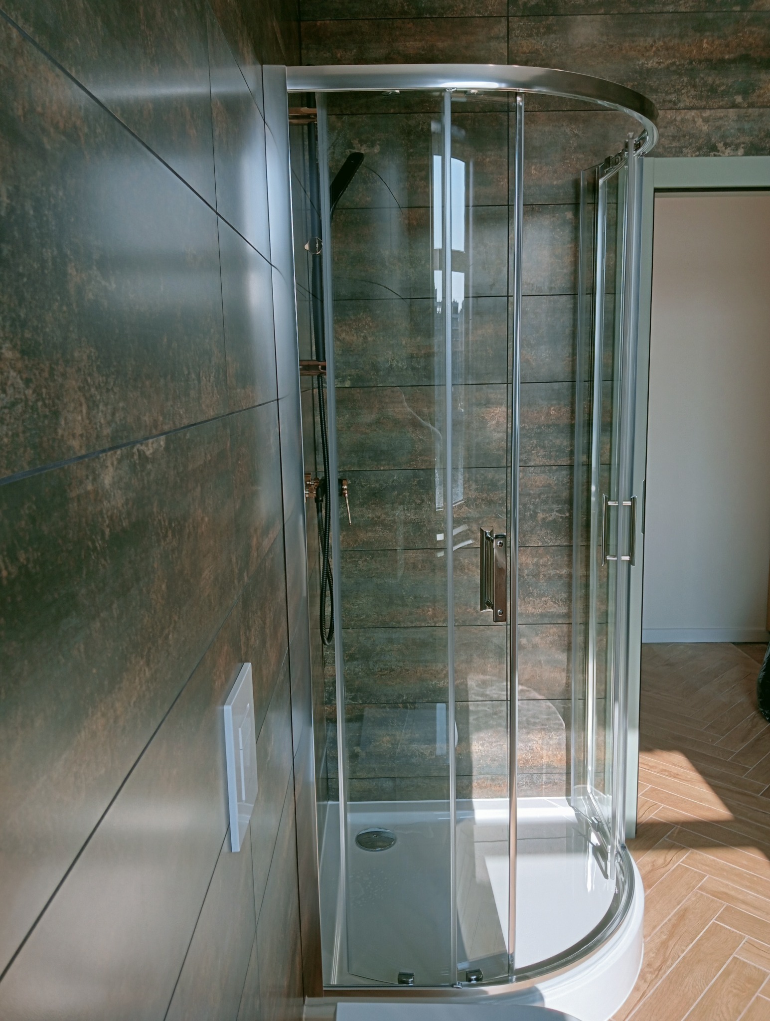 Nowoczesna kabina prysznicowa z przesuwnymi drzwiami, wykończona brązowymi płytkami imitującymi drewno, z widoczną armaturą i odpływem liniowym.