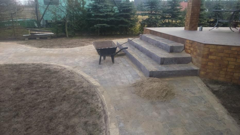 Ułożona kostka brukowa na ścieżce i schodach w Kamieniu Krajeńskim, z taczką i stertą piasku obok.