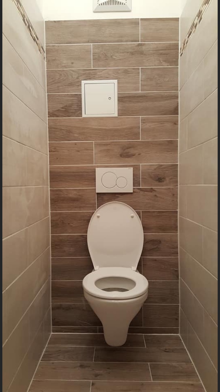 Wąska toaleta wykończona płytkami imitującymi drewno, z ukrytą spłuczką i otworem rewizyjnym.