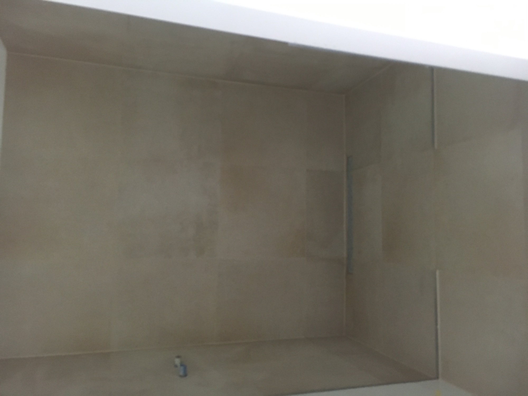 Wnętrze łazienki w trakcie prac, wyłożone beżowymi płytkami ceramicznymi, z widocznymi śladami fugowania i drobnymi zabrudzeniami na podłodze.