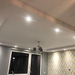 Darex - Sufit podwieszany z oświetleniem punktowym i ozdobnym żyrandolem w pokoju z szarą ścianą i tapetą w geometryczne wzory.