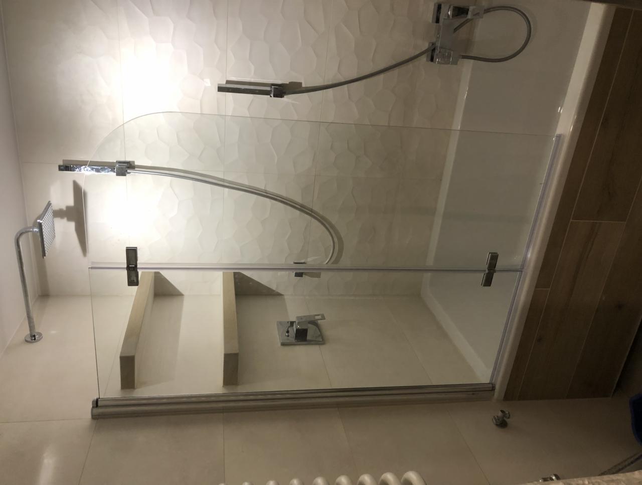 Kabina prysznicowa z półokrągłą szybą, chromowaną armaturą i szarymi płytkami z delikatną fakturą, widok z góry na dół.