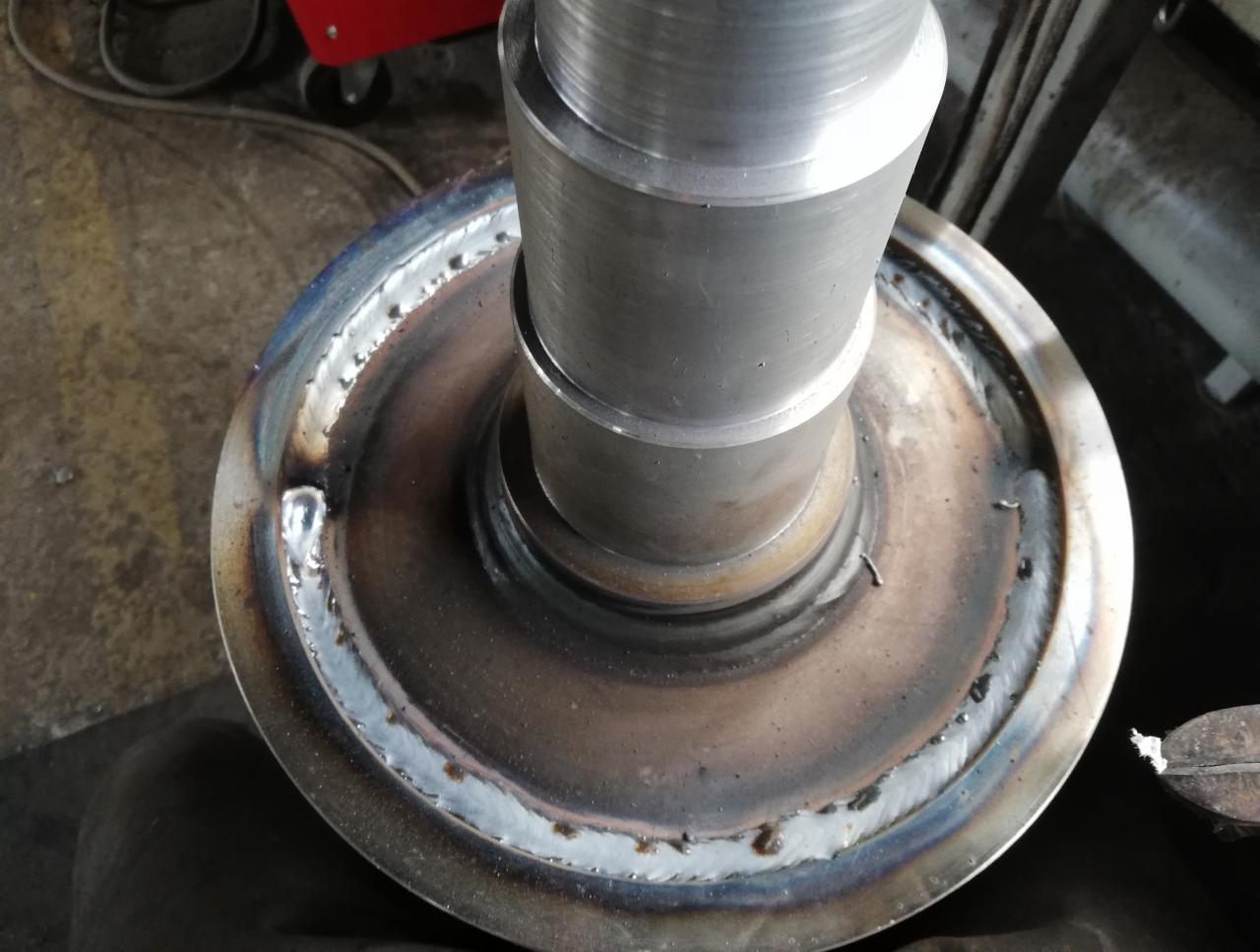 Metalowy element z widocznym spoiną po spawaniu, na tle warsztatu z wózkiem spawalniczym