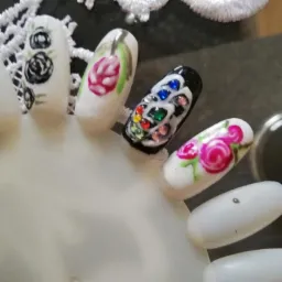 Wzornik z tipsami prezentujący zdobienia paznokci: czarne róże, różowy tulipan, abstrakcyjne białe wzory na czarnym tle z kolorowymi kryształkami, różowe róże, wykonane w Nakle nad Notecią.