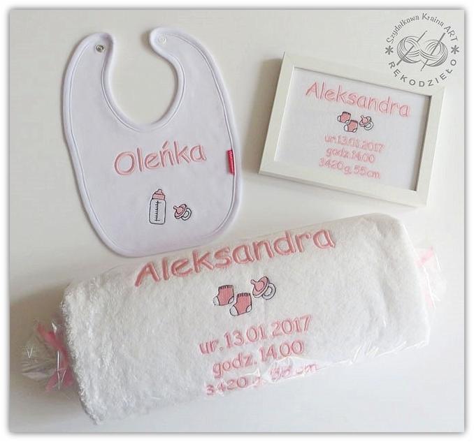 Biały śliniak dziecięcy z imieniem Oleńka i haftowanymi symbolami butelki i smoczka, obok ręcznik z wyhaftowanym imieniem Aleksandra i datą urodzenia oraz ramka z wyhaftowanymi danymi urodzenia...