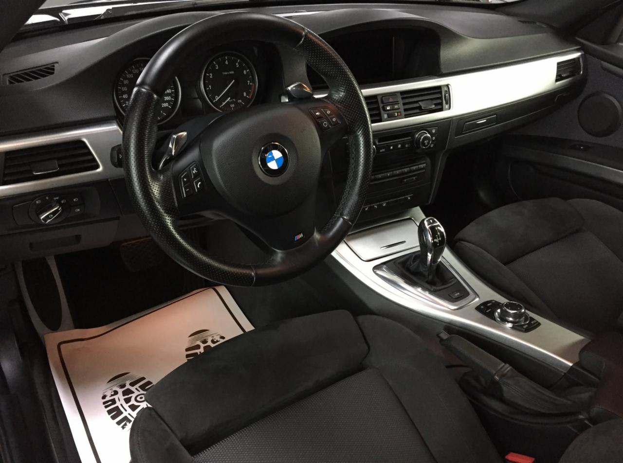 Wnętrze samochodu BMW w Chrzanowie, widoczna kierownica z logo, deska rozdzielcza z srebrnymi elementami i czarne fotele. Na podłodze leży papierowa mata ochronna z nadrukiem śladów butów.