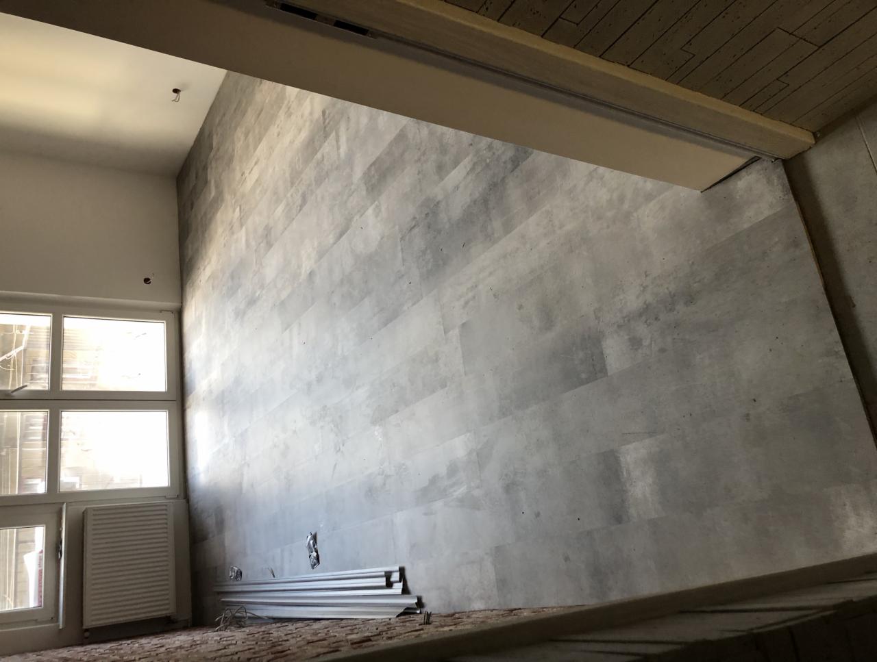 Ściana wykończona panelami imitującymi beton, widok z dołu, okno z grzejnikiem, listwy przypodłogowe czekają na montaż.