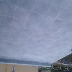 Szare płytki ceramiczne ułożone na podłodze tarasu, widoczne elementy budynku i otoczenia.