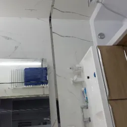 Nowoczesna łazienka z białymi marmurowymi płytkami, drewnianą szafką pod umywalką i lustrem odbijającym grzejnik z niebieskim ręcznikiem.