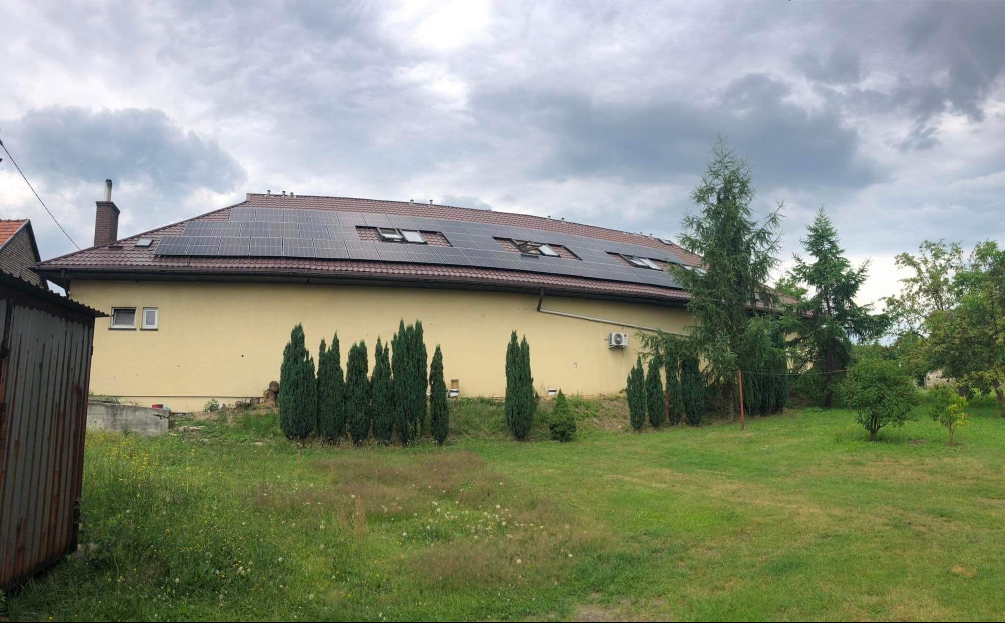 Dom jednorodzinny z panelami słonecznymi na dachu, widok z ogrodu w pochmurny dzień.