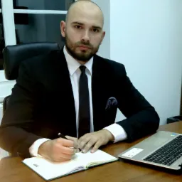 Portret mężczyzny w garniturze, siedzącego za biurkiem i piszącego w notatniku, z laptopem obok i oknem w tle.