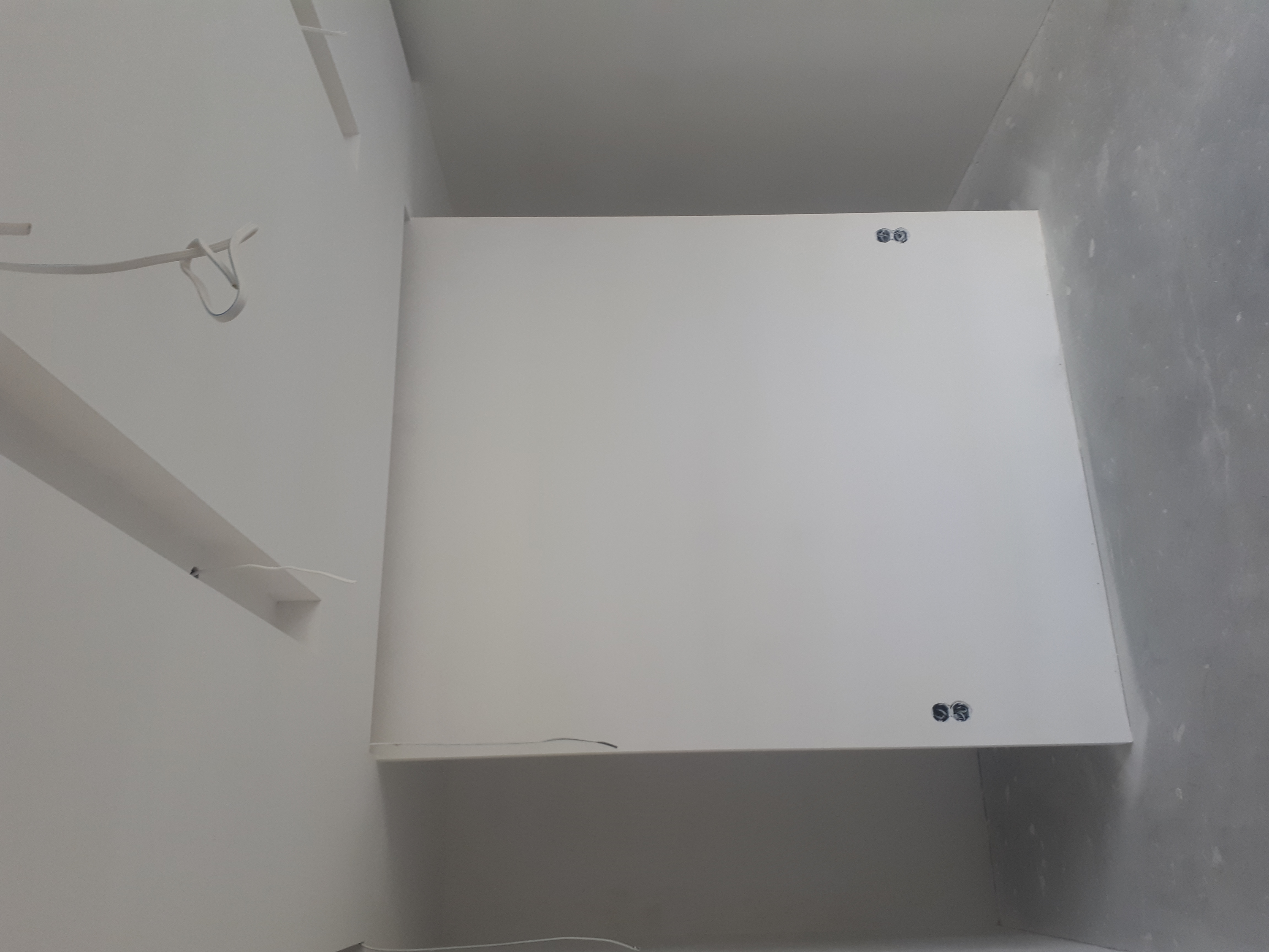 Montaż płyty karton gips na suficie, widoczne otwory na oświetlenie, surowe ściany w tle.