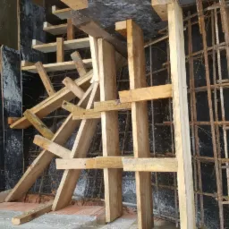 Szalunek schodów z drewnianych desek i stalowego zbrojenia w trakcie budowy, widoczne elementy konstrukcyjne i betonowa ściana w tle.