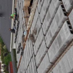 NewHome Łukasz Szkulimowski - Budowa ściany z szarych bloczków betonowych, widoczna stalowa siatka zbrojeniowa, dwóch pracowników w trakcie pracy, widok z góry.