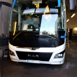 Przód autobusu MAN z nową szybą czołową, zabezpieczoną niebieską taśmą, w warsztacie.