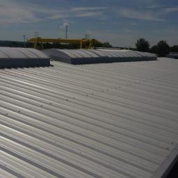 MiKAR - Długi, srebrny dach z blachy trapezowej z kilkoma świetlikami kopułowymi, widoczny suwnica bramowa w tle.