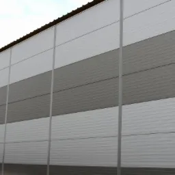 Szara ściana hali przemysłowej wykonana z paneli warstwowych ułożonych w poziome pasy o naprzemiennych odcieniach szarości, widoczna z dołu pod kątem.