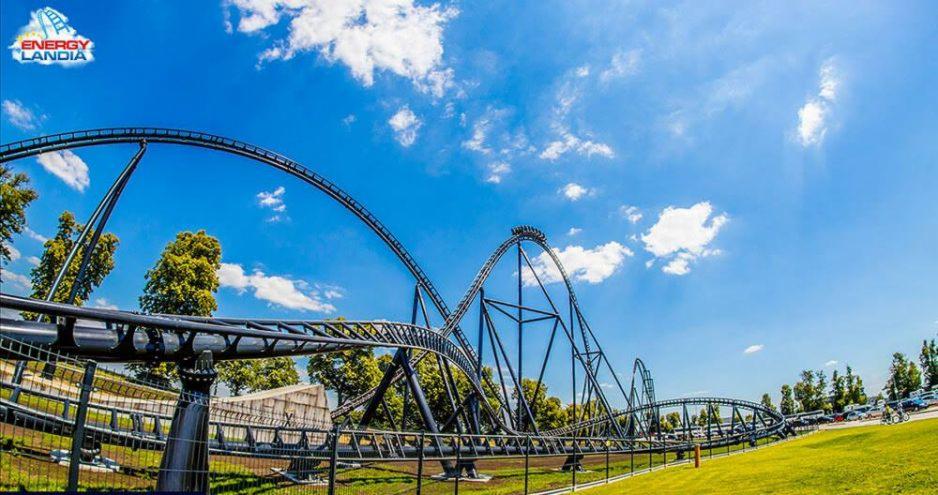 Wysoka kolejka górska z wagonikami na tle błękitnego nieba z obłokami, widok z dołu.