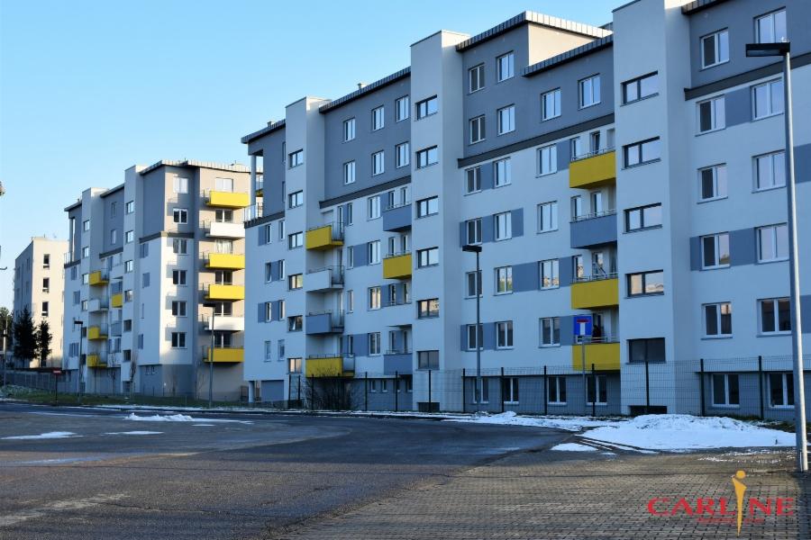 Nowoczesne budynki wielorodzinne z kolorowymi balkonami, widoczne z poziomu ulicy w pochmurny dzień.