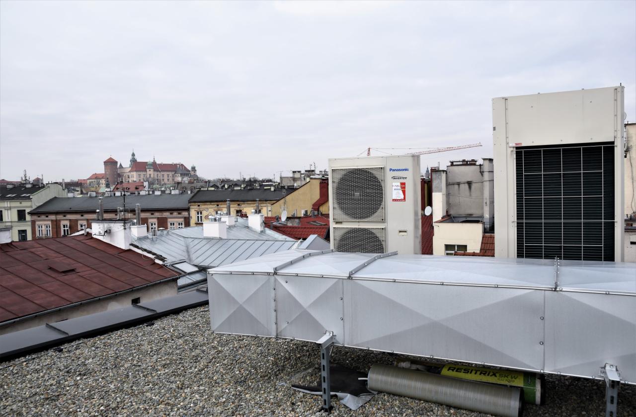 Instalacja wentylacyjna na dachu budynku z widokiem na panoramę miasta, w tle Wawel.