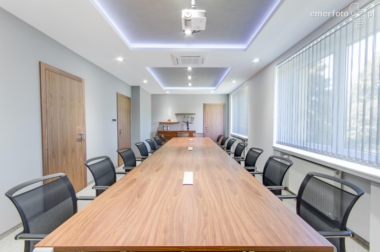 Sala konferencyjna z długim drewnianym stołem i czarnymi krzesłami w Zebrzydowicach, oświetlona lampami LED i projektorem sufitowym.