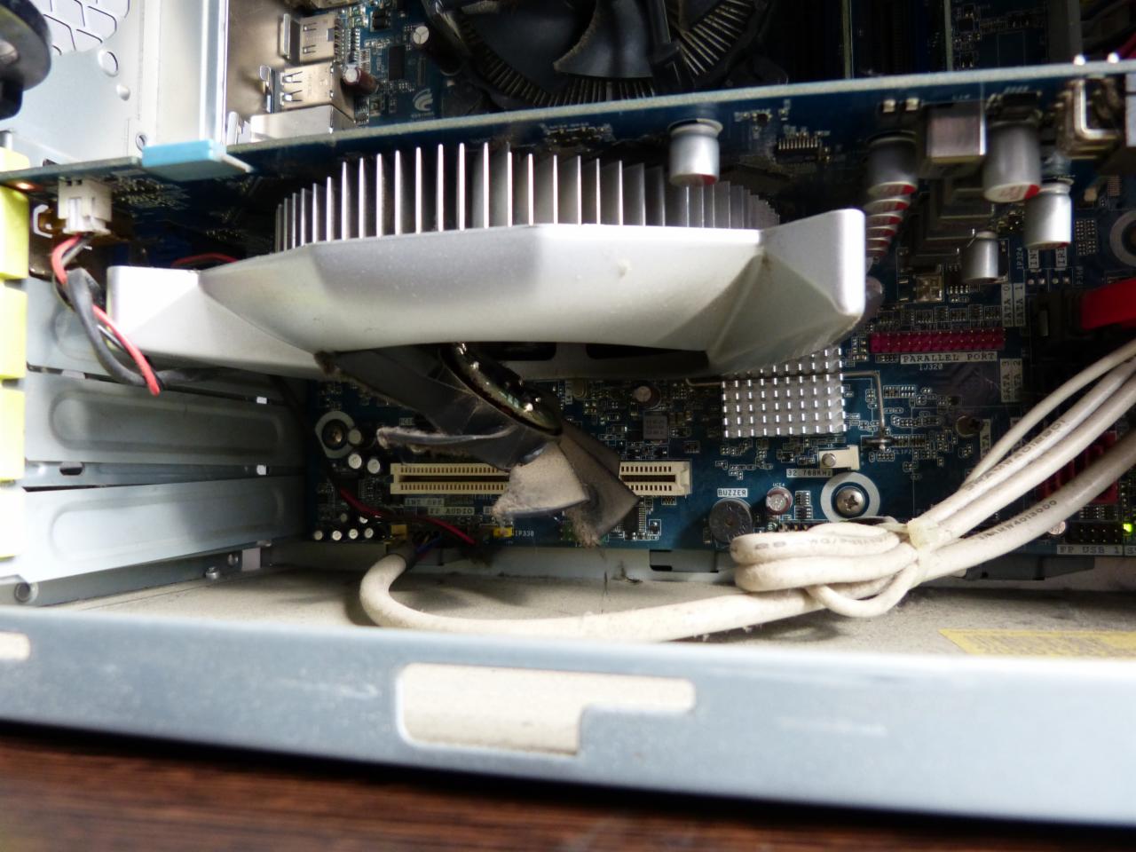 Wnętrze obudowy komputera stacjonarnego z widoczną kartą graficzną z radiatorem, płytą główną i kablami. Widoczny kurz i zabrudzenia wewnątrz obudowy.