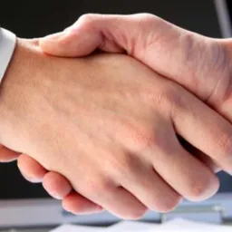 Uścisk dłoni dwóch osób na tle otwartego laptopa, symbolizujący zawarcie umowy lub partnerstwo biznesowe.