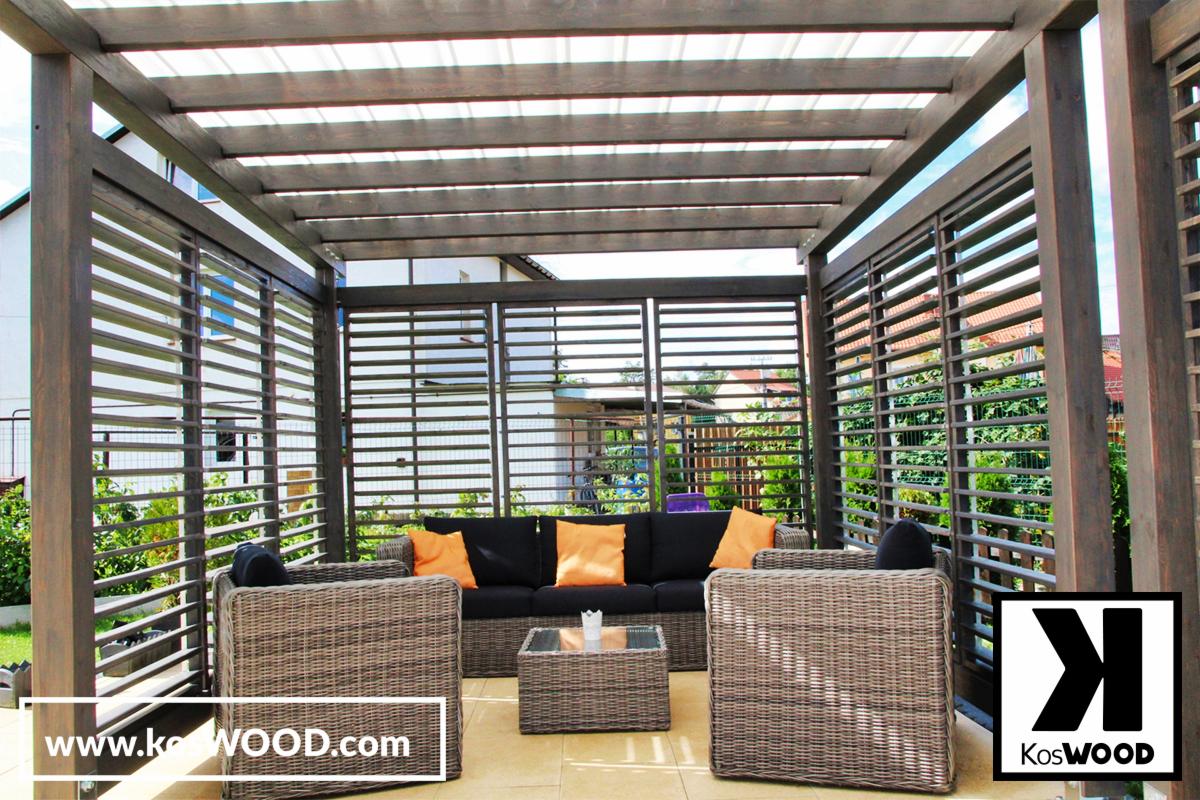 Zadaszona drewniana konstrukcja tarasowa z poziomymi listwami, wyposażona w rattanowe meble wypoczynkowe z pomarańczowymi poduszkami, logo firmy w prawym dolnym rogu.
