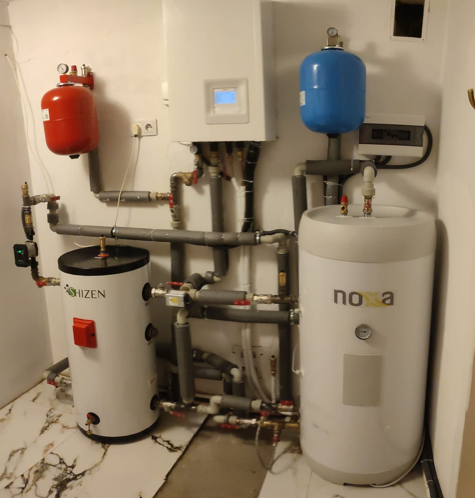 Dwa białe zbiorniki na wodę (Shizen i no a) z podłączonymi rurami i elementami instalacji w pomieszczeniu z marmurową podłogą.