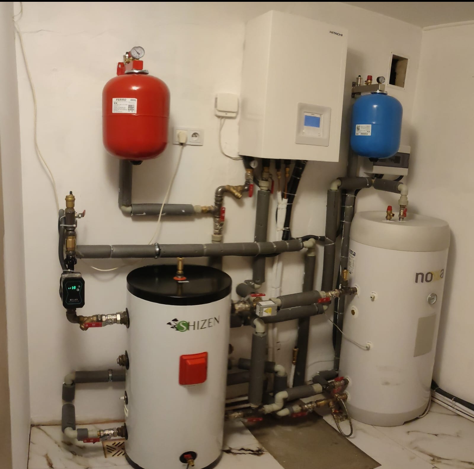 Kompleksowa instalacja grzewcza z kotłem Hitachi, zbiornikiem Shizen i zbiornikami wyrównawczymi Ferro w pomieszczeniu technicznym z marmurową podłogą.