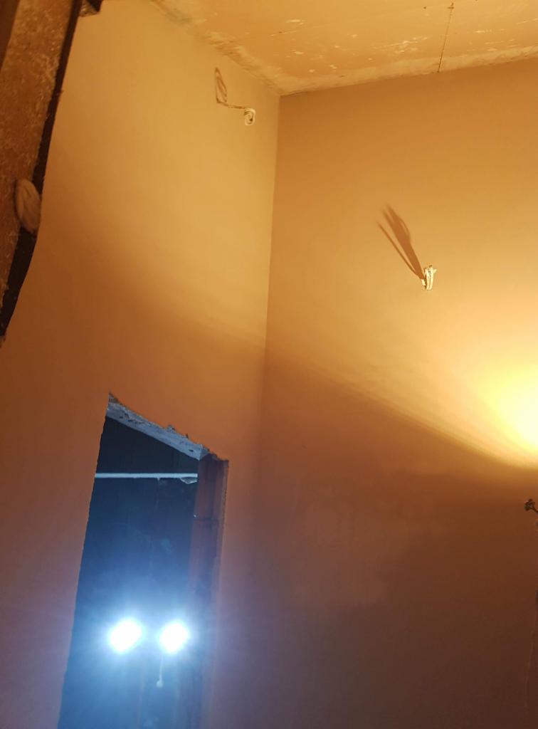 Ściany i sufit po nałożeniu gładzi gipsowej, widoczne gniazdka elektryczne i niedokończone obramowanie drzwi.