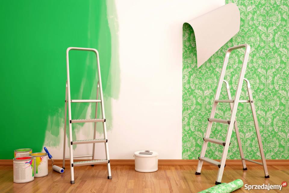 Ściana w trakcie odnawiania: fragment pomalowany na zielono, obok fragment z zieloną tapetą, drabiny, puszki z farbą i wałek malarski na drewnianej podłodze.