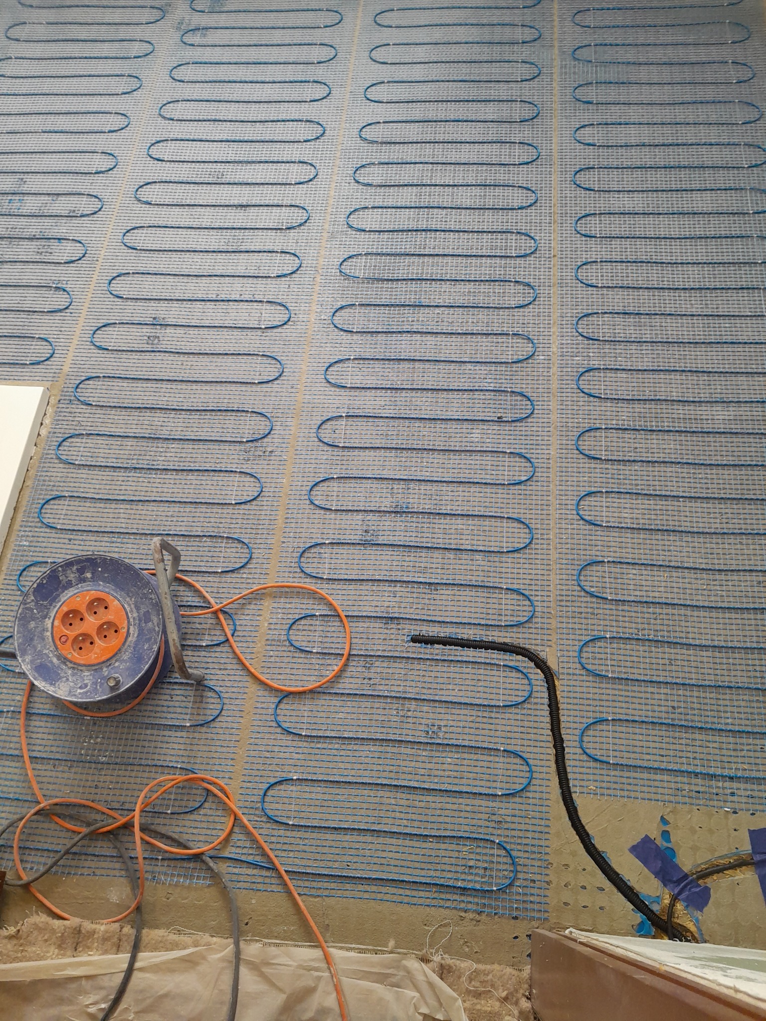 Rozłożona mata grzewcza na podłodze z widocznym przewodem zasilającym i przedłużaczem bębnowym.