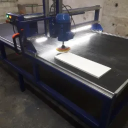 Niebieska maszyna do obróbki kamienia z zamontowaną szczotką polerską, biały element roboczy na czarnym blacie.