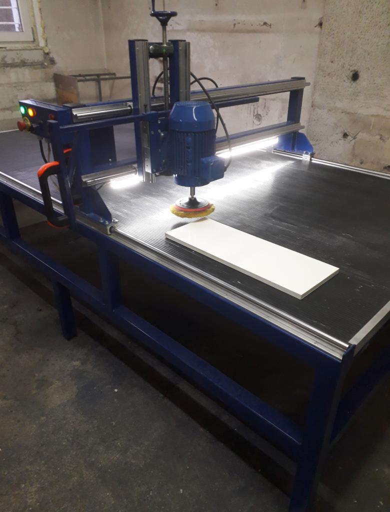 Niebieska maszyna do obróbki kamienia z zamontowaną szczotką polerską, biały element roboczy na czarnym blacie.