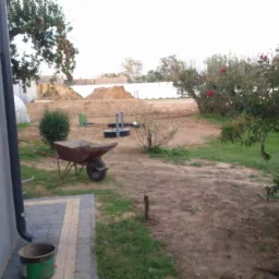 Teren posesji w trakcie prac ziemnych, widoczna taczka, wykop i elementy instalacji kanalizacyjnej, przygotowany pod budowę. W tle roślinność i ogrodzenie.