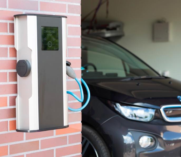 Stacja ładowania samochodu elektrycznego zamontowana na ceglanej ścianie garażu, podłączona do czarnego BMW i3.