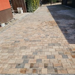 Max-Bud - Ułożona kostka brukowa w odcieniach beżu i szarości tworzy wzór na podjeździe. W tle widoczny budynek i ogrodzenie, a z boku narzędzia i wiaderka.