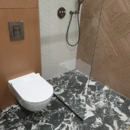 Nowoczesna łazienka z białą wiszącą toaletą, marmurową podłogą, kabiną prysznicową ze szklaną ścianką i panelami dekoracyjnymi na ścianie.