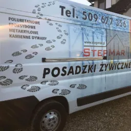 Biały samochód dostawczy z reklamą firmy STEPMAR, oferującej m.in. posadzki poliuretanowe, epoksydowe, metakrylowe i kamienne dywany, z numerem telefonu i adresem strony internetowej.