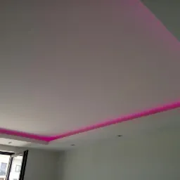 Nowoczesny sufit podwieszany z oświetleniem LED w kolorze fuksji, widok z dołu na tle okna balkonowego.