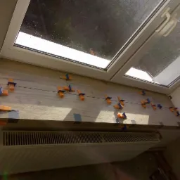 Montaż drewnopodobnych paneli na parapecie okna dachowego, z użyciem poziomicy i klipsów dystansowych, nad grzejnikiem.