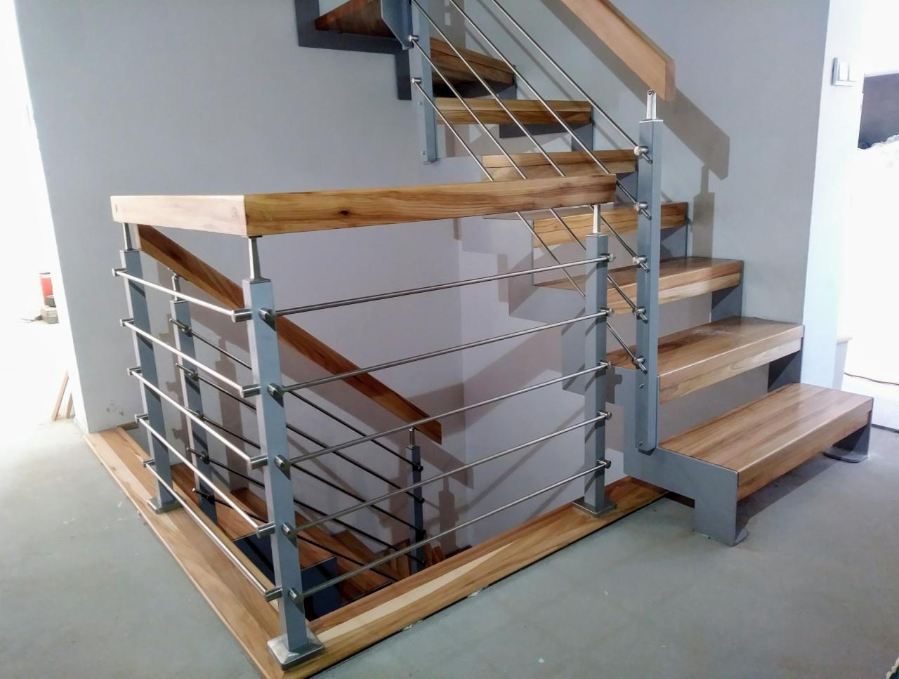 Nowoczesne schody z drewnianymi stopniami i balustradą ze stali nierdzewnej w domu w Puńcowie, widok z dołu.